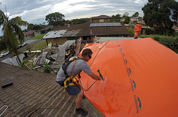 Person on roof attaching a large platic sheet to a roof using a hand tool. Person on roof attaching a large platic sheet to a roof using a hand tool.
