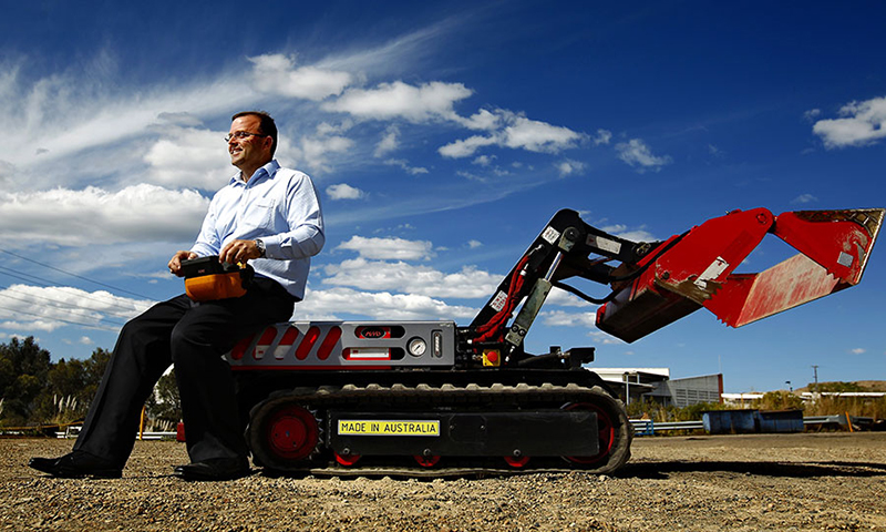 Person sitting on a low tracked vehicle the size of a couch. It has a large hinged jaw on the front. Person sitting on a low tracked vehicle the size of a couch. It has a large hinged jaw on the front.