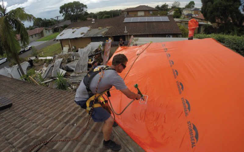 Person on roof attaching a large platic sheet to a roof using a hand tool. Person on roof attaching a large platic sheet to a roof using a hand tool.