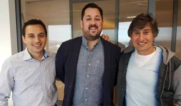 Three men posing for a photo in front of glass windows Three men posing for a photo in front of glass windows