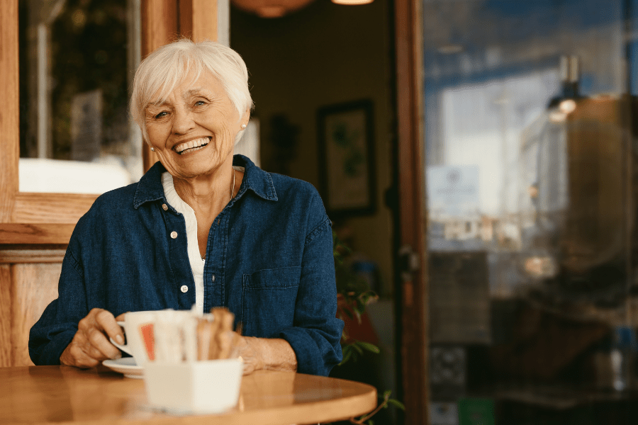 Smiling woman with white hair sits at a table in a coffee shop
