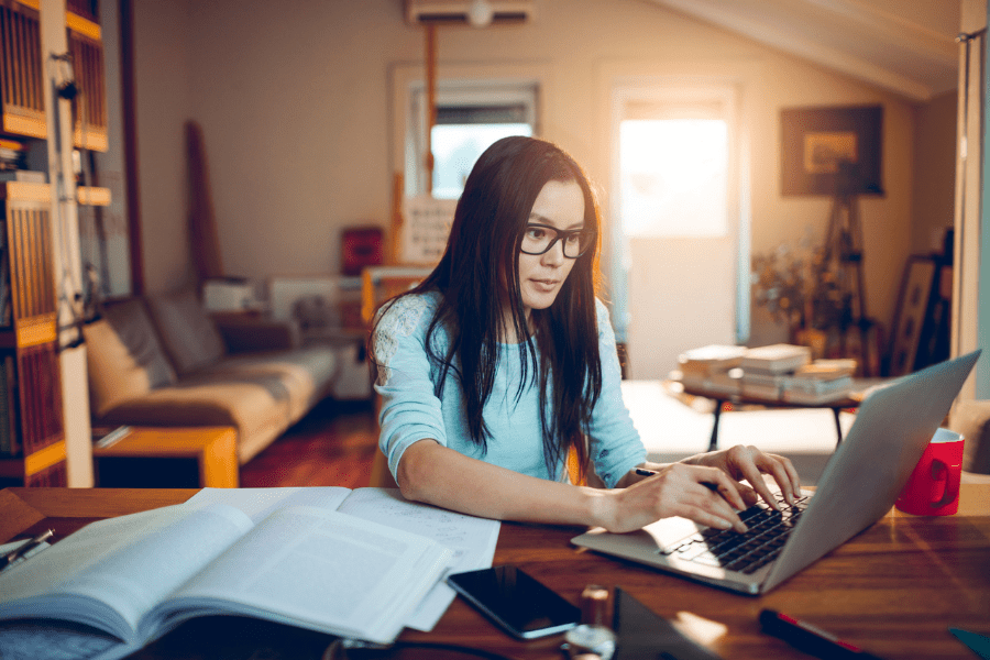 A woman types on her laptop next to books