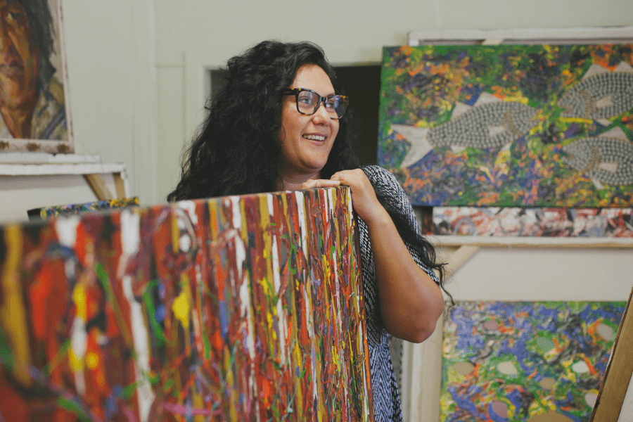 An Australian First Nations woman in a studio surrounded by paintings