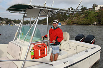 Brightly coloured plastic device attached to the side of a small boat. It is similar in size and shape to a briefcase, but with a cylinder shaped part connected to one side.