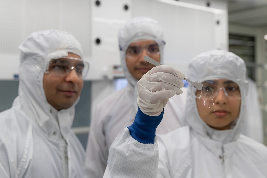 three lab technicians in contamination overalls, 1 holding a medical device