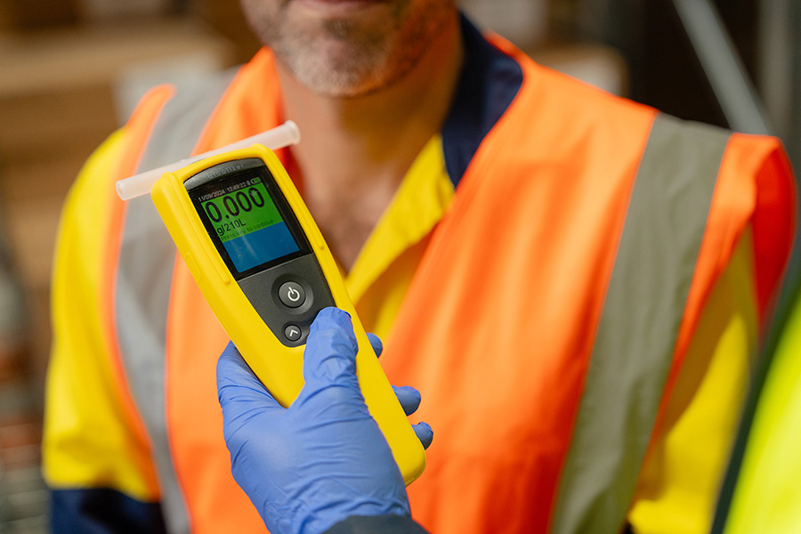 Image of a person presenting an Alcolizer testing device to a man in a high vis vest.