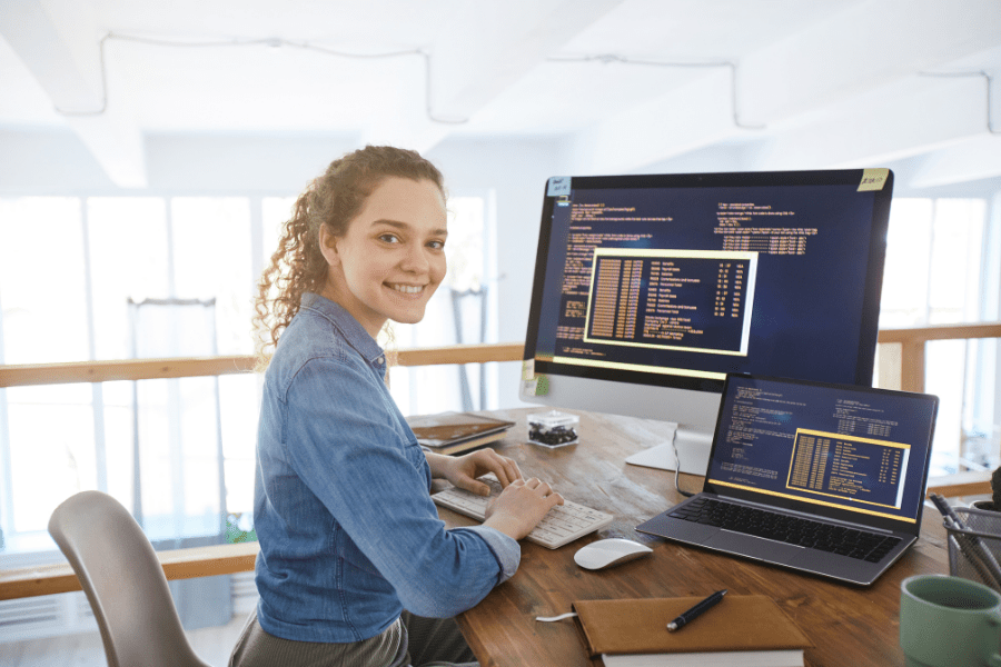 A women sitting in front of 2 computers with code across the screens.