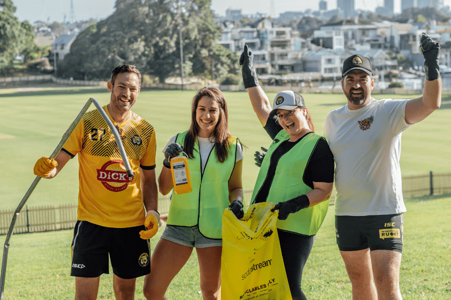Four smiling adults pick up rubbish in a field